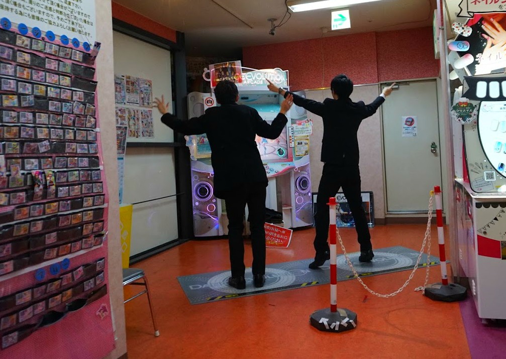 Two Japanese teenage boys dancing in front of a fun machine in Akihabara