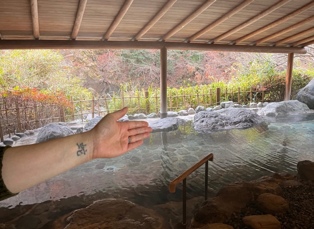 Cory pointing at the onsen with her wrist tattoo visible