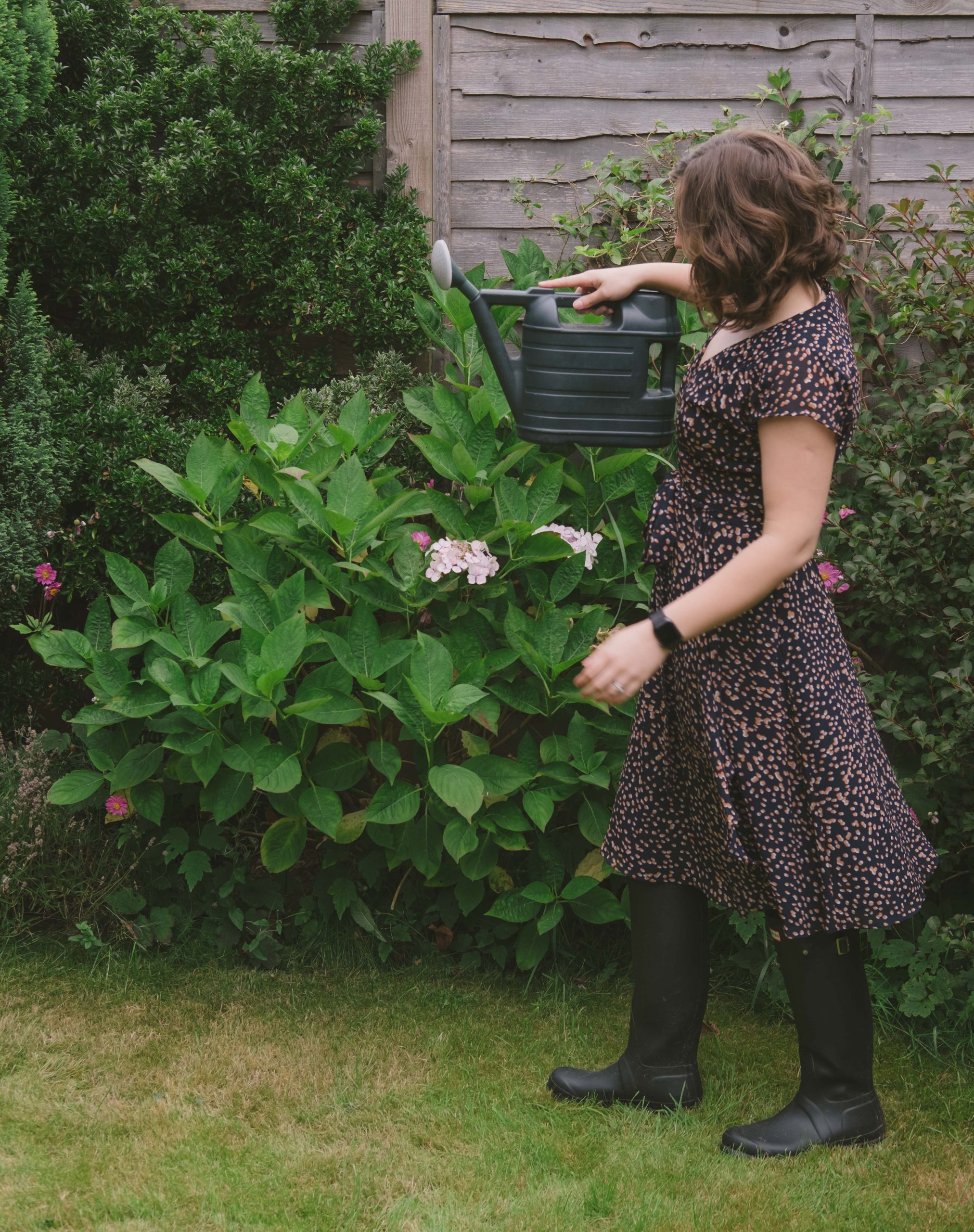Cory wearing her Aries dress from Bluffworks and watering the plants in a garden during a staycation in the UK