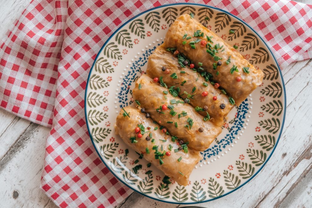 An image of traditional Romanian sarmale, showcasing succulent cabbage rolls filled with a flavorful mixture of minced meat, rice, and herbs, served on a plate with a side of creamy polenta and a dollop of sour cream, garnished with fresh dill, representing a beloved comfort food in Romanian cuisine