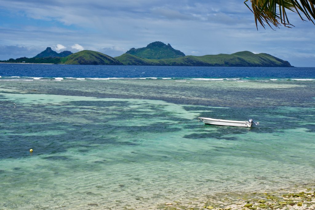 Fiji Island beach with boat, mountains in the distance