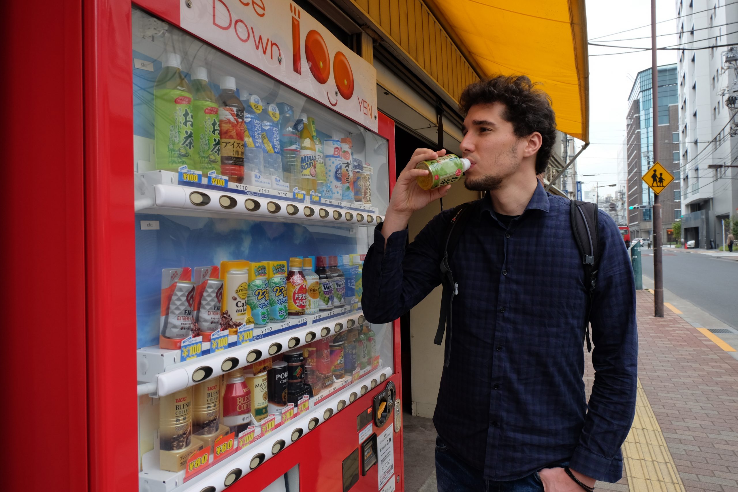 Greg drinking a bottled tea at a vending machine in Japan