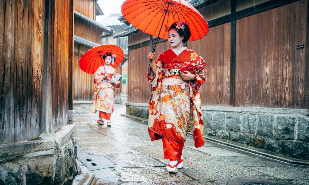 Two geishas in traditional kimono holding red umbrellas, exploring the traditional Gion district