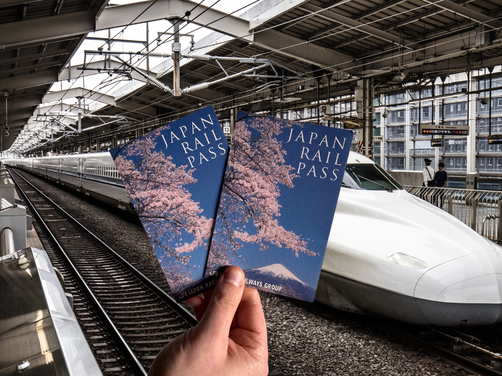 Greg holding our Japan rail passes in front of a Shinkansen in Japan