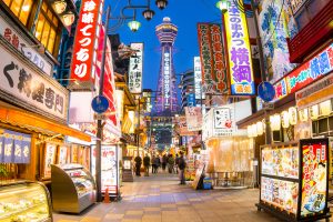 Lively Osaka street with shops and food stalls. The Tsutenkaku Tower in the background.