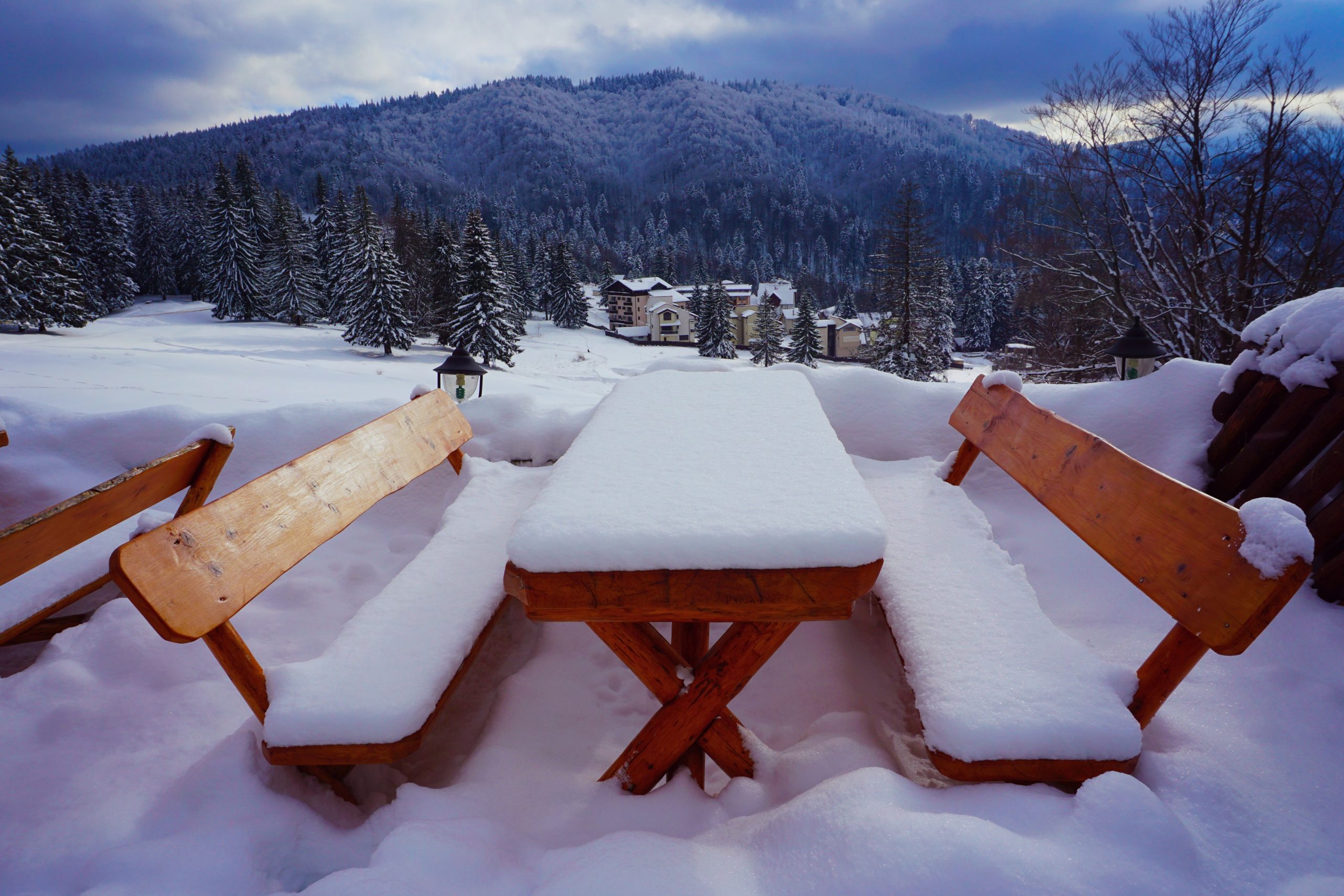 Snow on a wooden rustic bench overlooking the gorgeous mountain peaks in Poiana Brasov