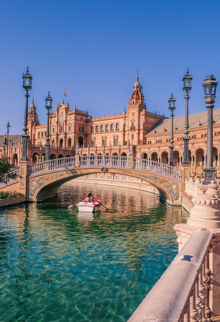 A couple in a boat, rowing on the main Seville canal, in front of Plaza de España