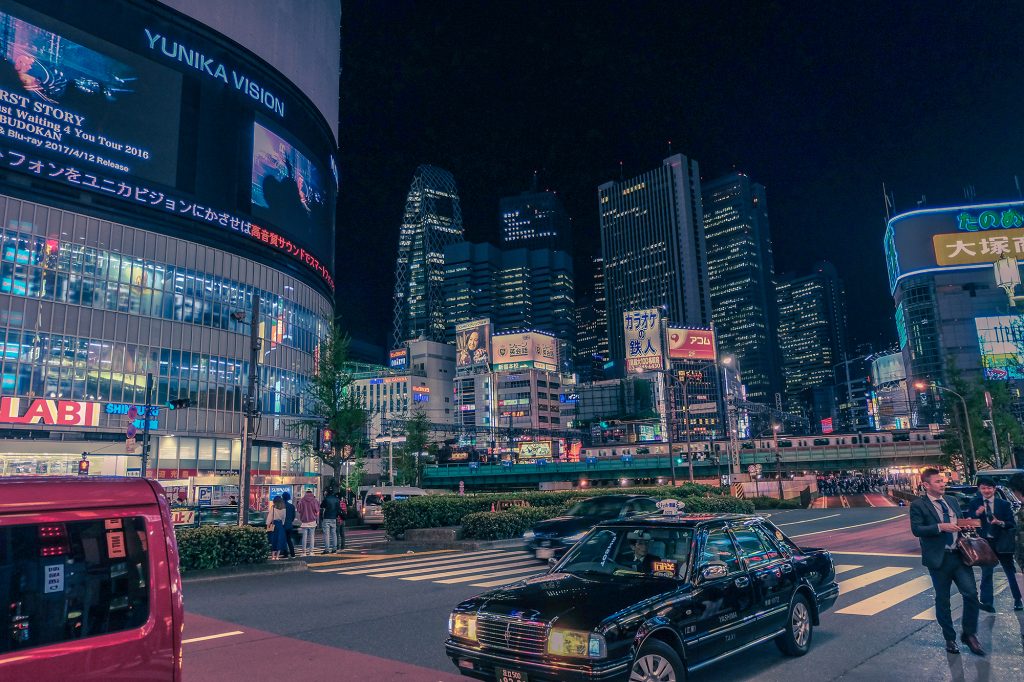 Outside the Shinjuku station at night, surrounded by skyscrapers and neon lights