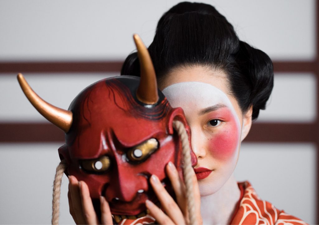 Woman with geisha makeup holding a Japanese mask