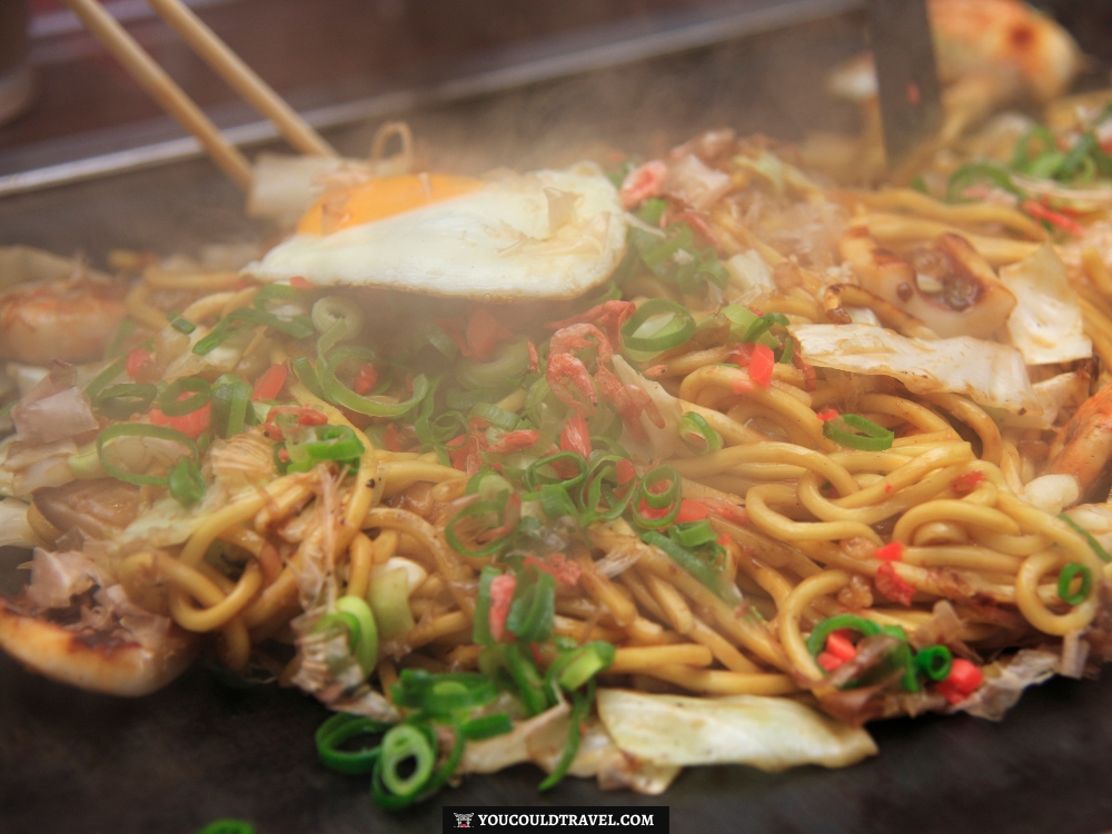 Yakisoba being prepared on a hot griddle and mixed with veg and meat